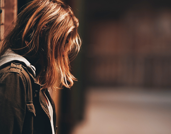 Jeune fille accotée à un mur, triste