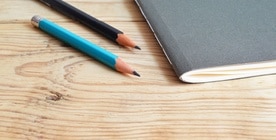 Deux crayons posés à côté d'un cahier, sur une table